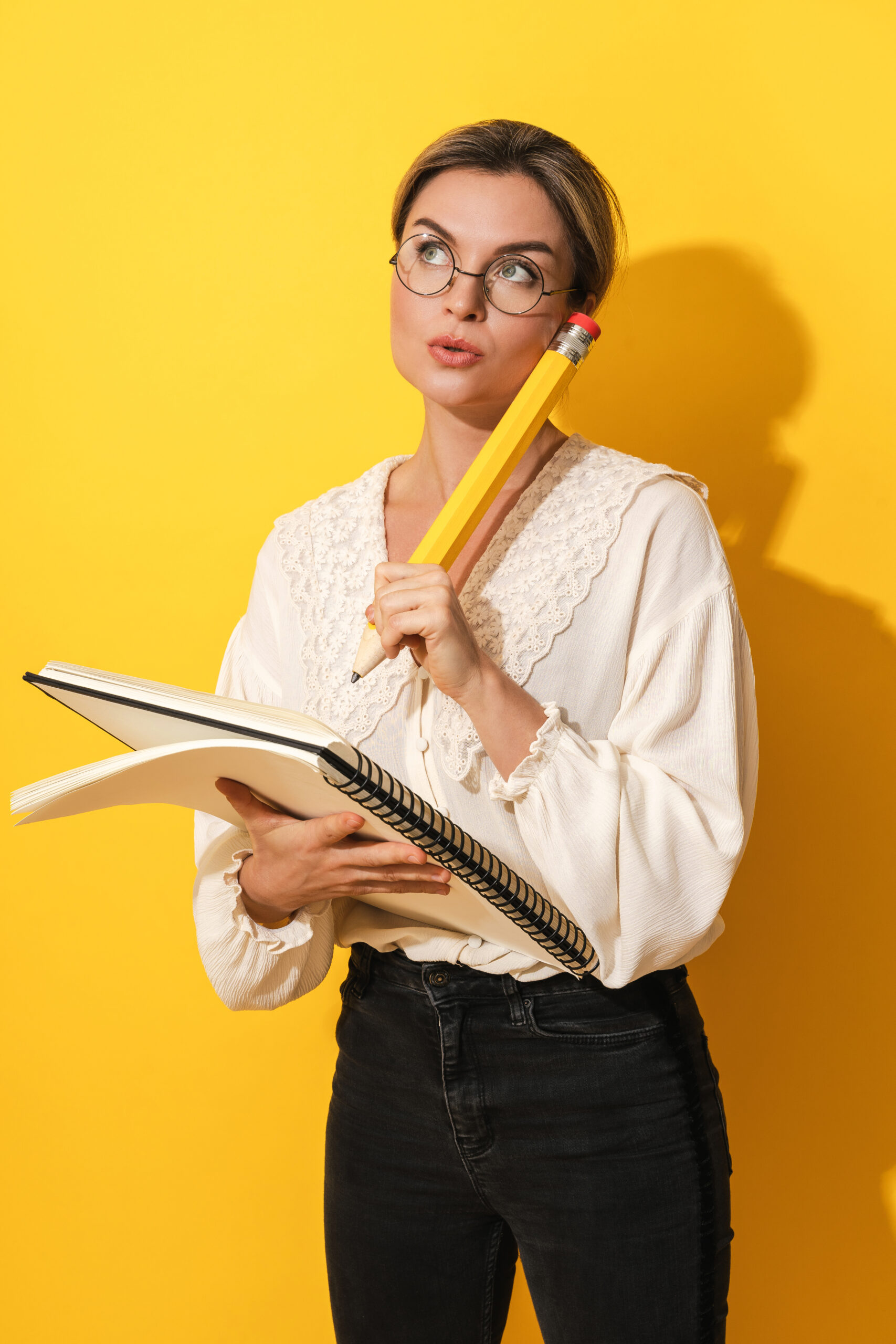 thoughtful woman wearing glasses holding big pencil and notebook